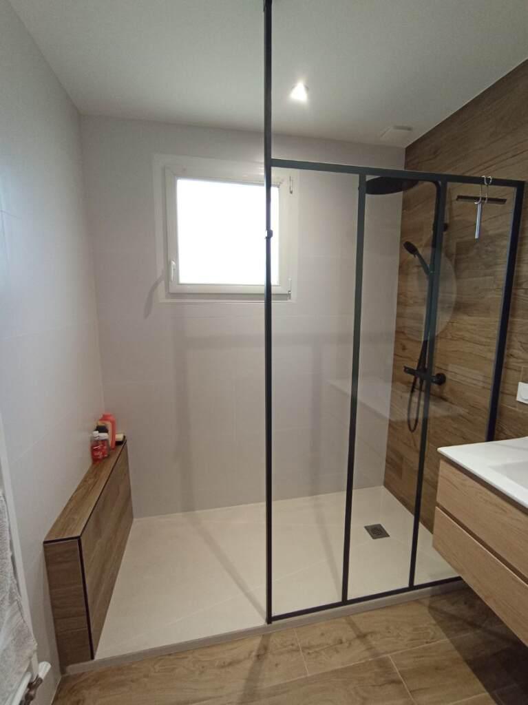 Salle de bains moderne avec une douche, des touches de bois, un élégant revêtement mural, une fenêtre blanche et des articles de toilette bien rangés sur une étagère en bois encastrée.