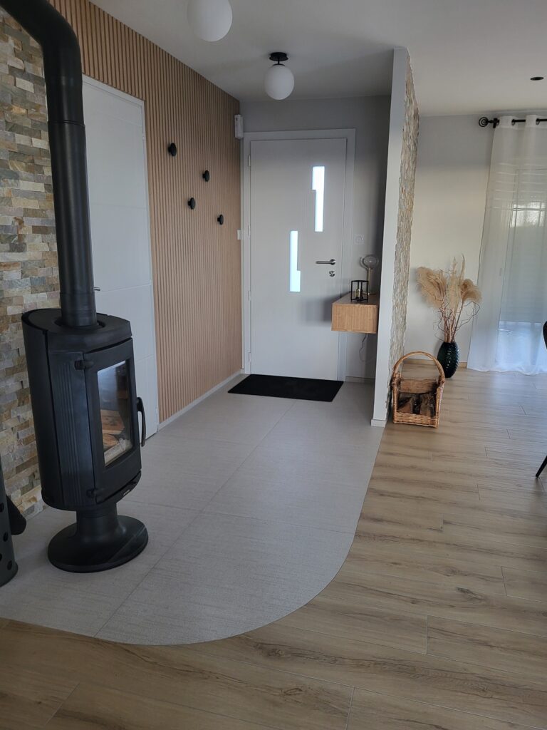 Entrée moderne avec un sol en bois clair et des accents de carrelage, un poêle à bois noir, une porte d'entrée blanche avec des panneaux en verre, une petite étagère murale, des paniers et des vases décoratifs.