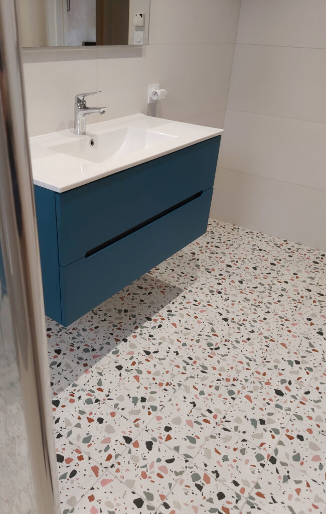 Une salle de bain moderne présente un meuble-lavabo mural bleu avec un évier et un robinet blancs au-dessus d'un carrelage salle de bain terrazzo élégant.