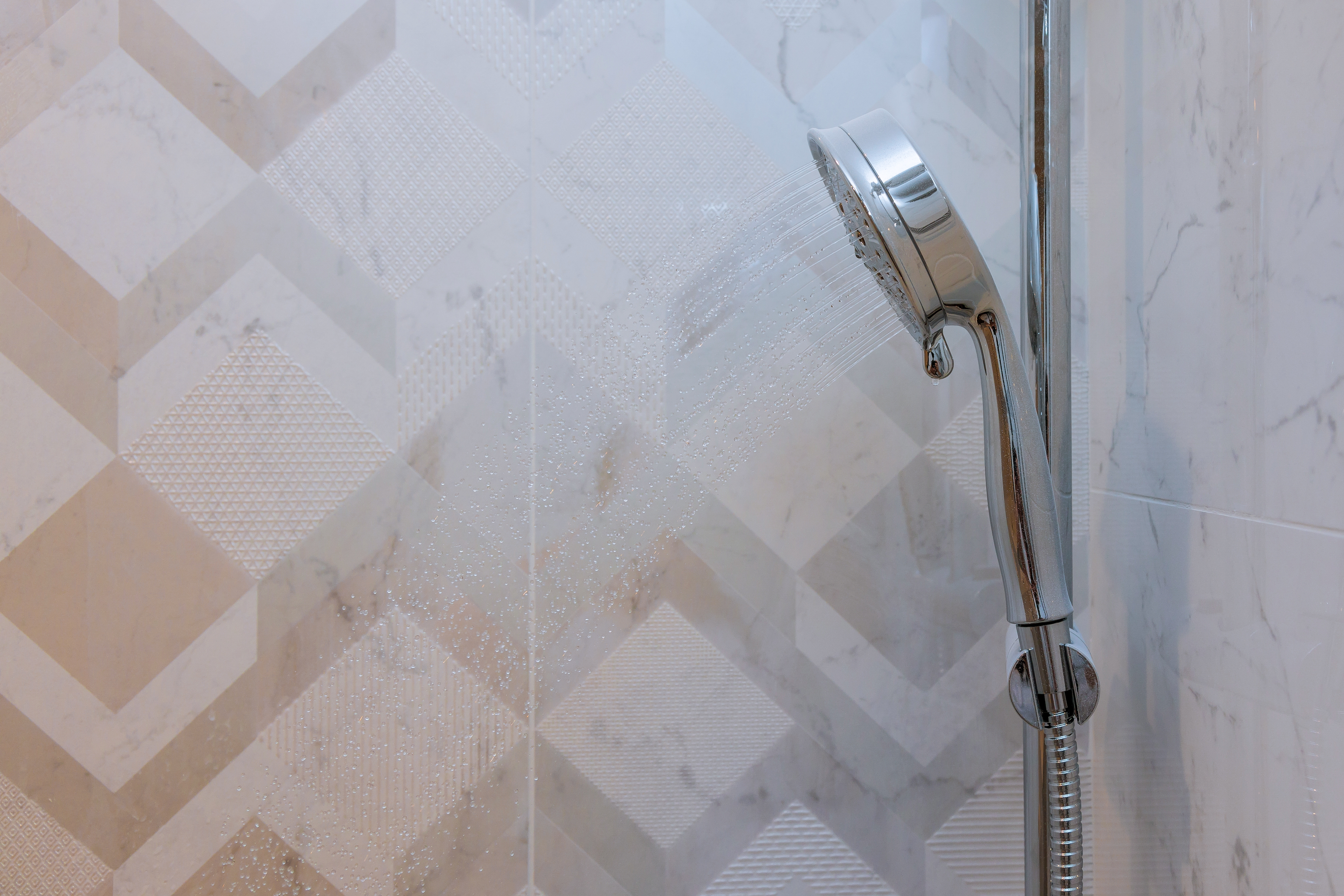 Une douchette pulvérise de l'eau sur un mur de salle de bains carrelé avec un motif en chevron.
