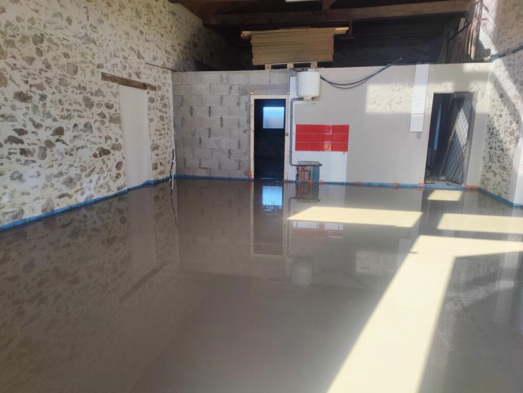 Une pièce aux murs de pierre et à l'intérieur partiellement inachevé, avec un sol en béton humide fraîchement coulé, reflétant l'environnement.